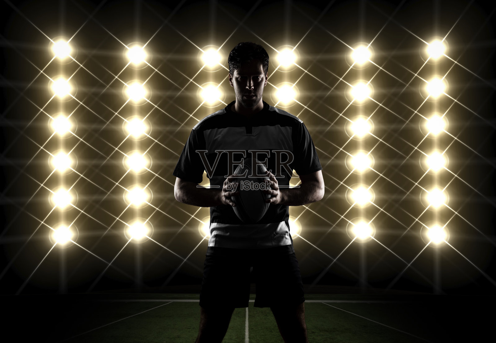 在体育场灯光前用球给橄榄球运动员投阴影照片摄影图片