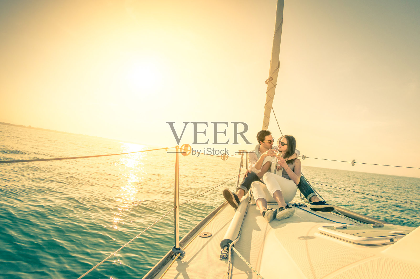 日落时分，年轻的情侣在帆船上喝着香槟相爱照片摄影图片