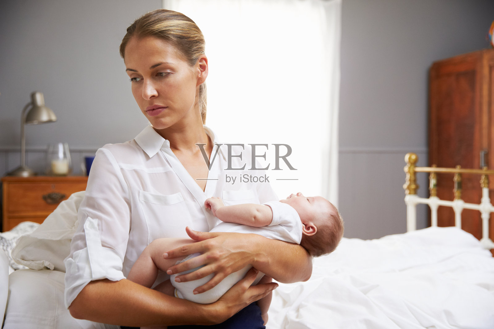 不快乐的母亲穿着工作服在卧室里抱着婴儿照片摄影图片