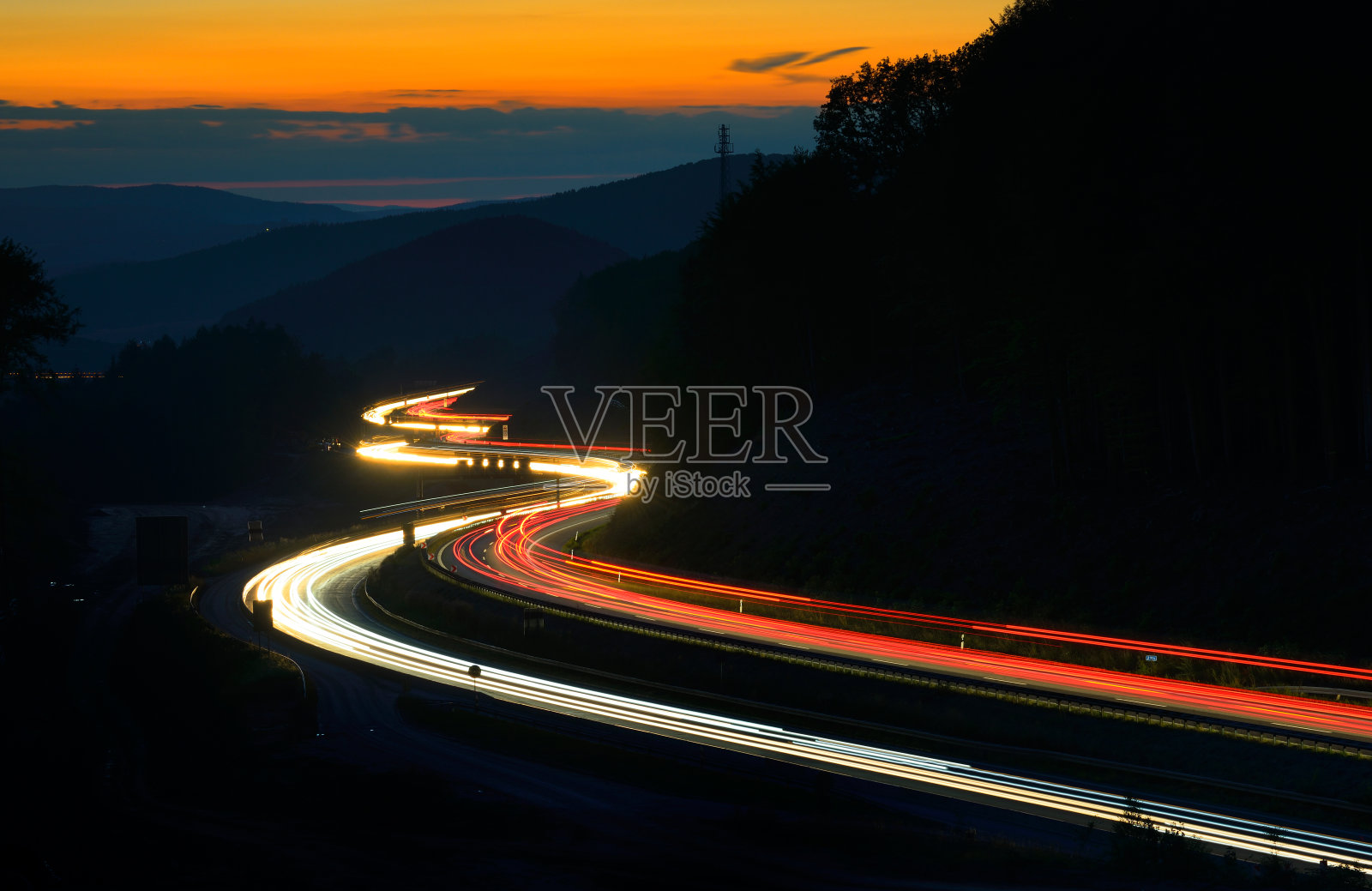 夕阳下，高速公路上蜿蜒的山峦上的车灯长时间曝光照片摄影图片