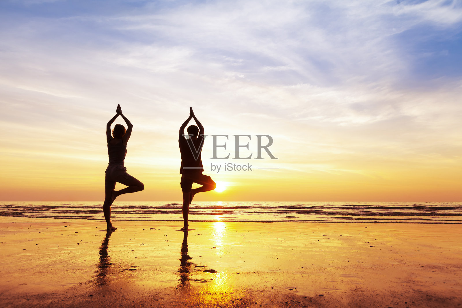 两人在沙滩上的树下练习瑜伽姿势，夕阳西下照片摄影图片