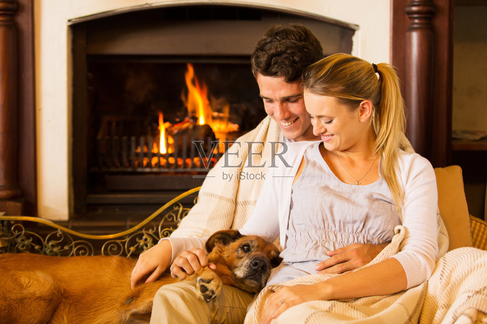 一对年轻夫妇和他们的宠物狗坐在壁炉旁照片摄影图片