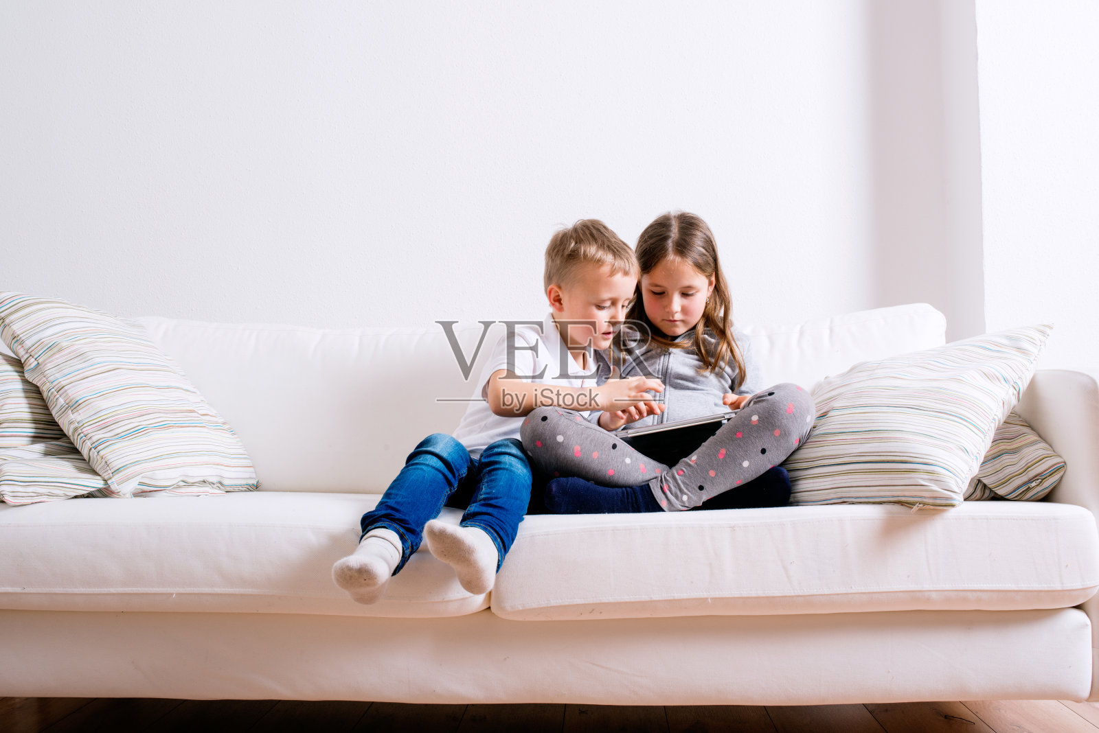 孩子们坐在家里的沙发上，玩着平板电脑照片摄影图片