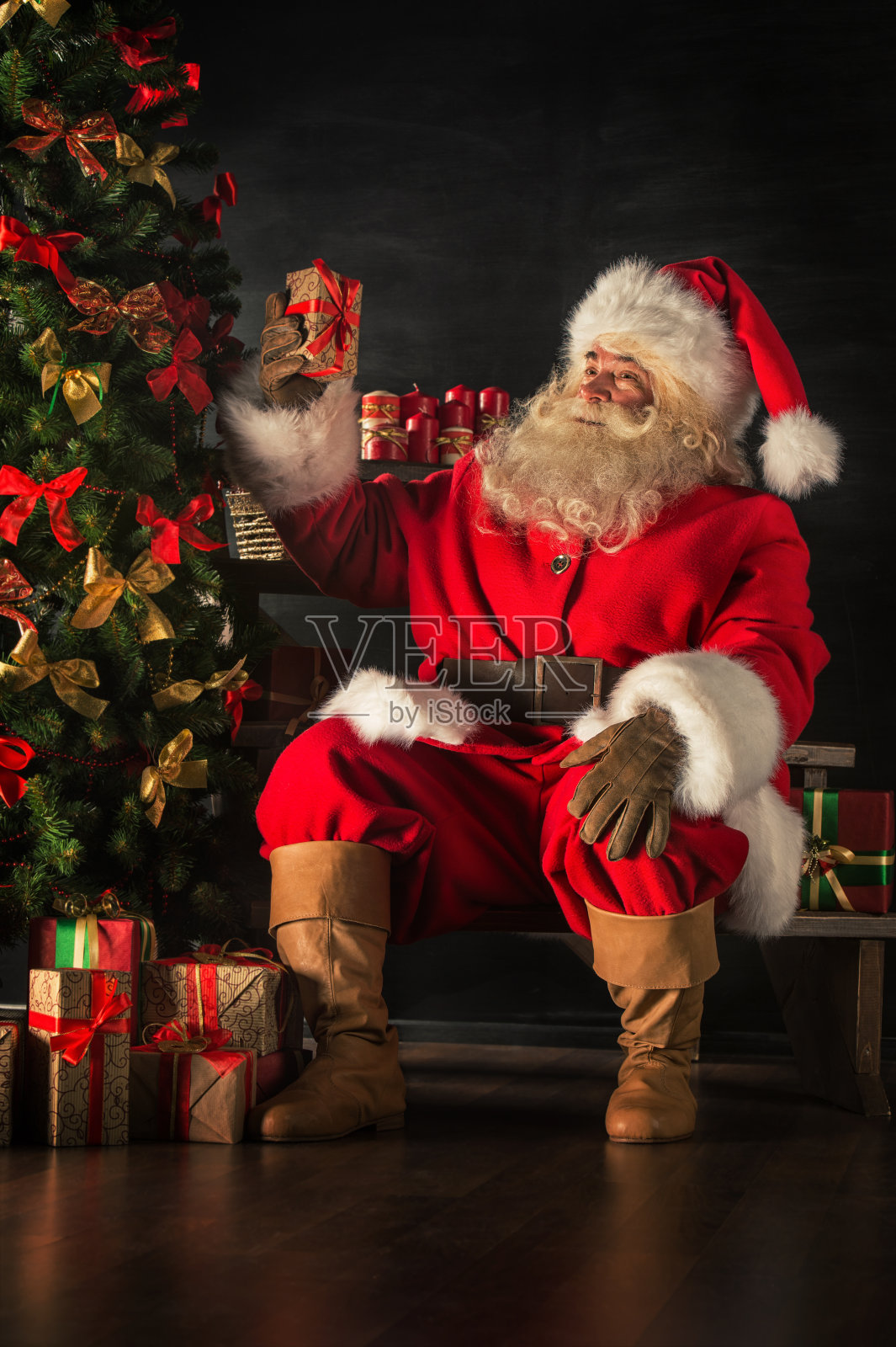 圣诞老人正在把礼物盒放在圣诞树下照片摄影图片