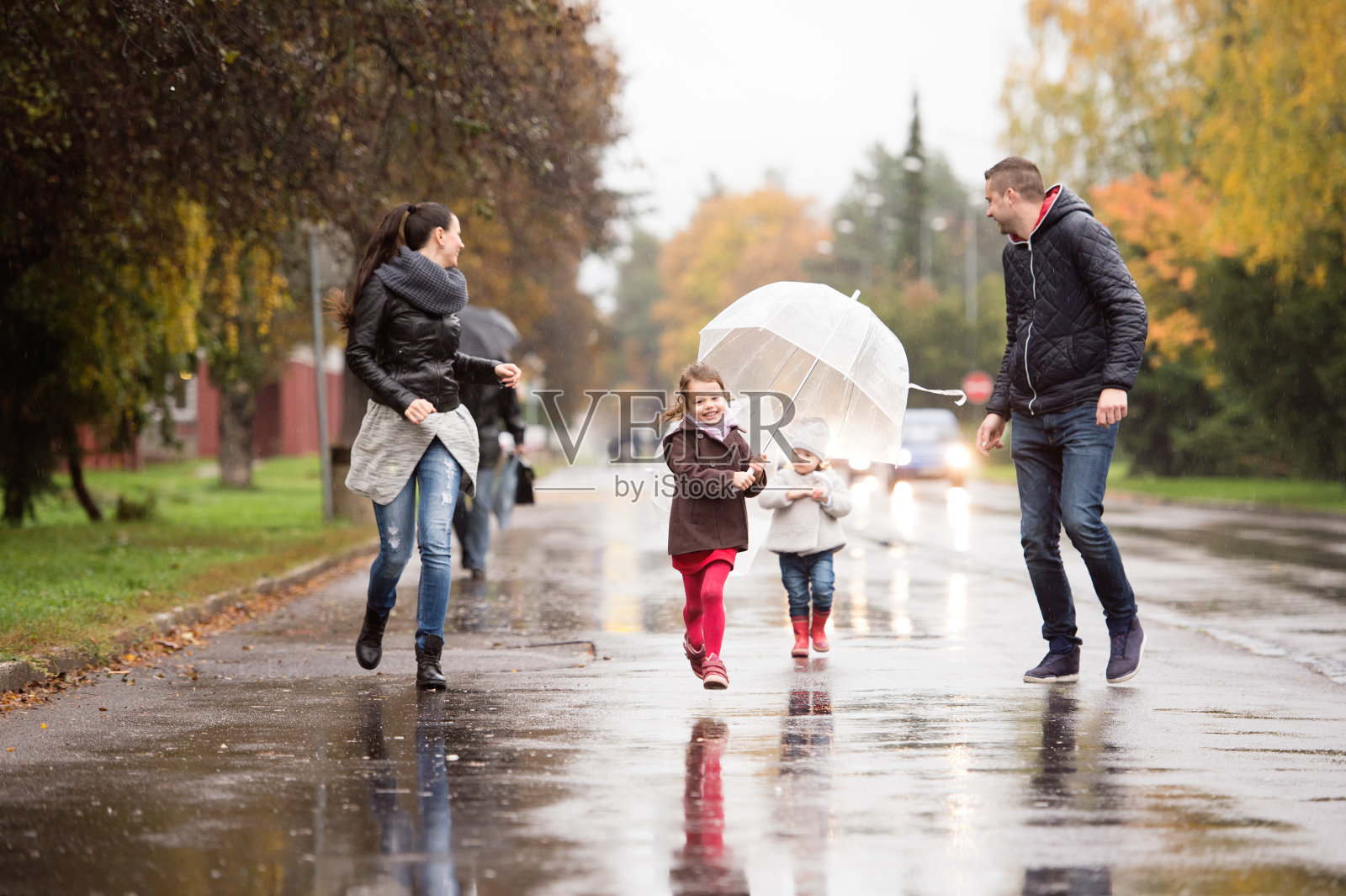 家人带着女儿撑着伞，奔跑着。雨天。照片摄影图片
