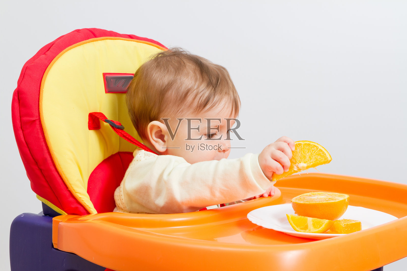 婴儿坐在橙色的高脚椅上。照片摄影图片
