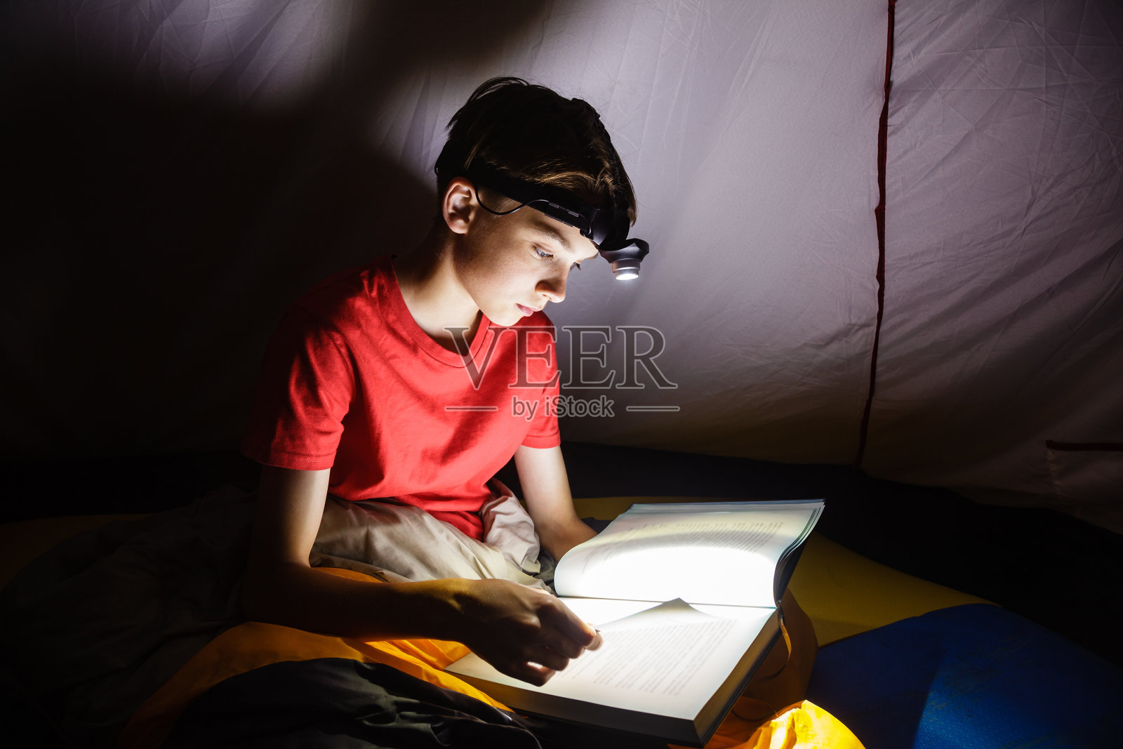 男孩在晚上用手电筒看书照片摄影图片
