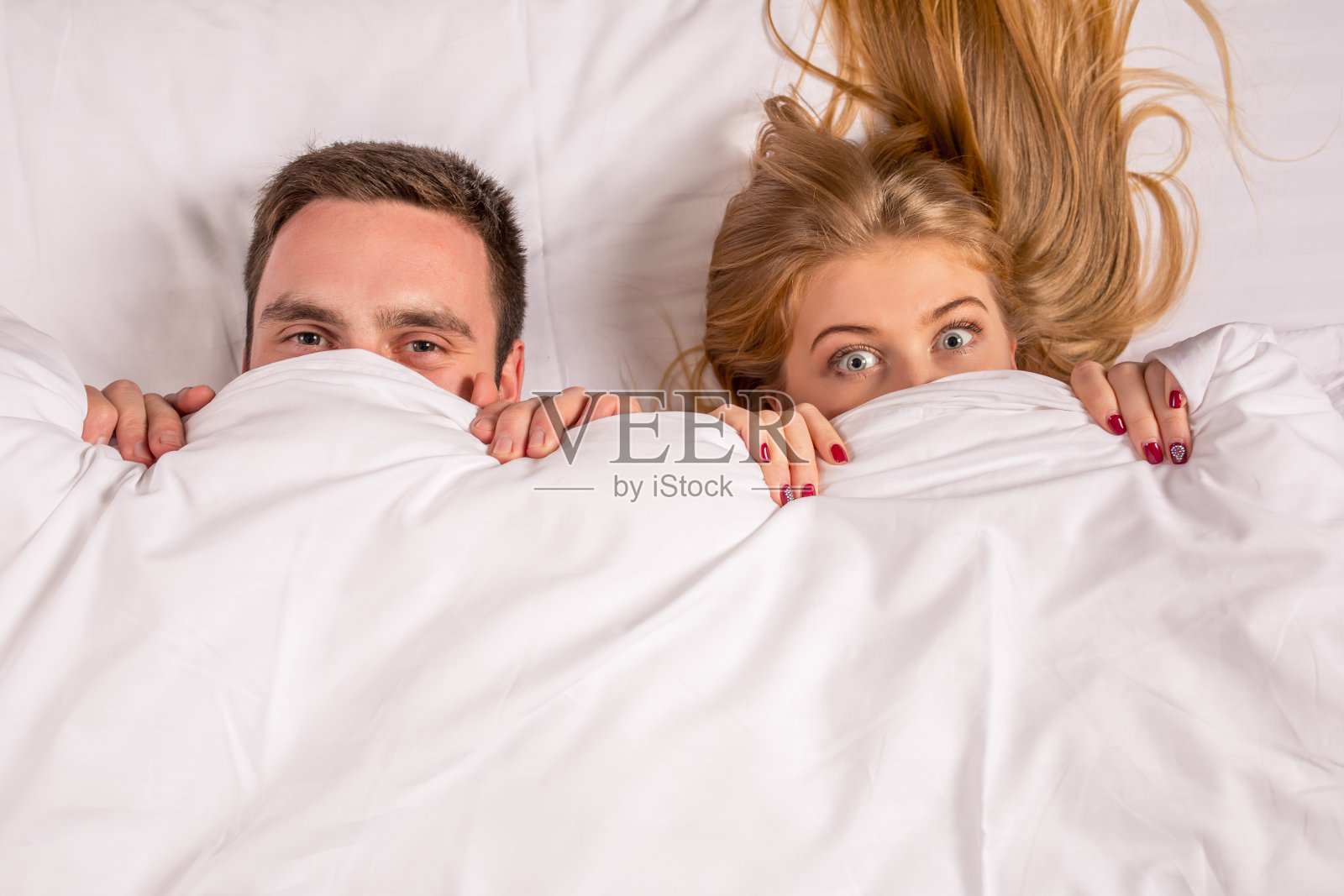 一对可爱的年轻夫妇躺在床上，看着照相机照片摄影图片
