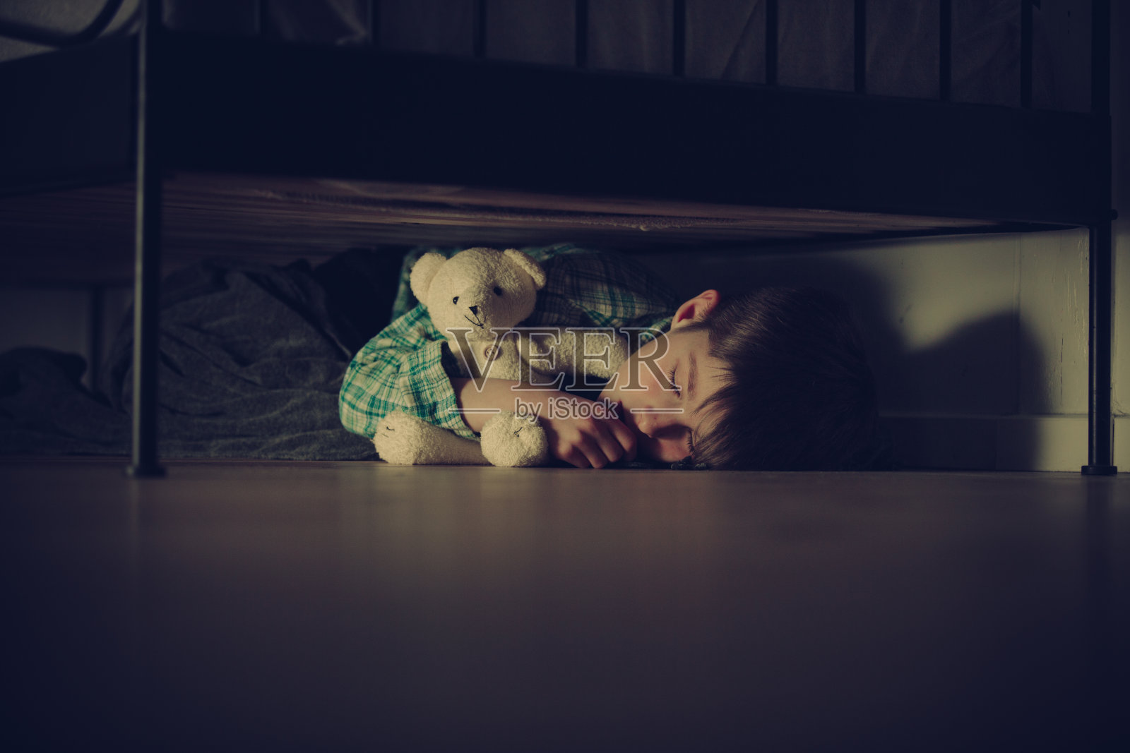 和泰迪熊一起睡在床下的受惊男孩照片摄影图片