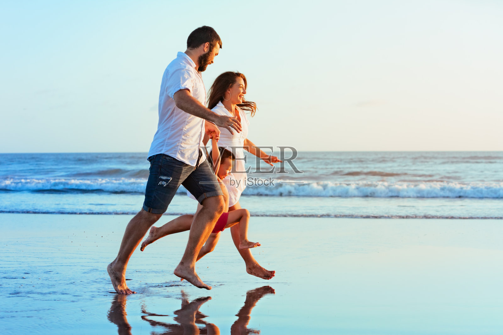 家庭-爸爸，妈妈，宝宝在日落海滩上跑步照片摄影图片