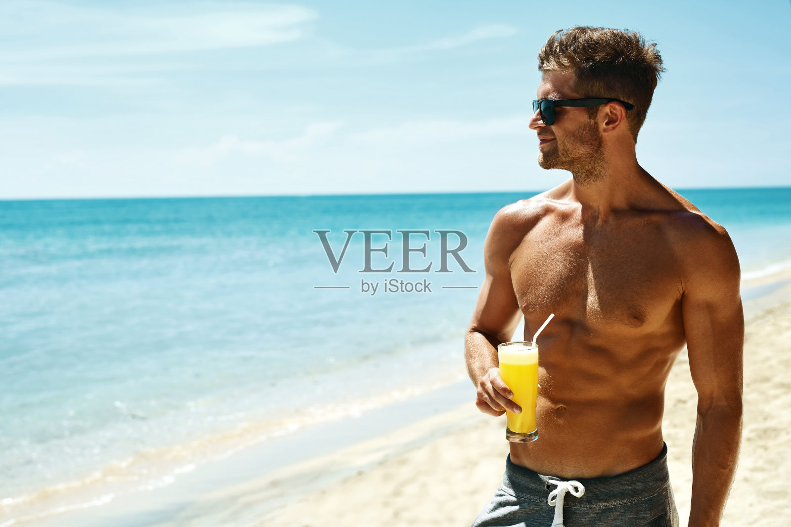 夏天。运动员肌肉男在海滩上喝果汁鸡尾酒照片摄影图片