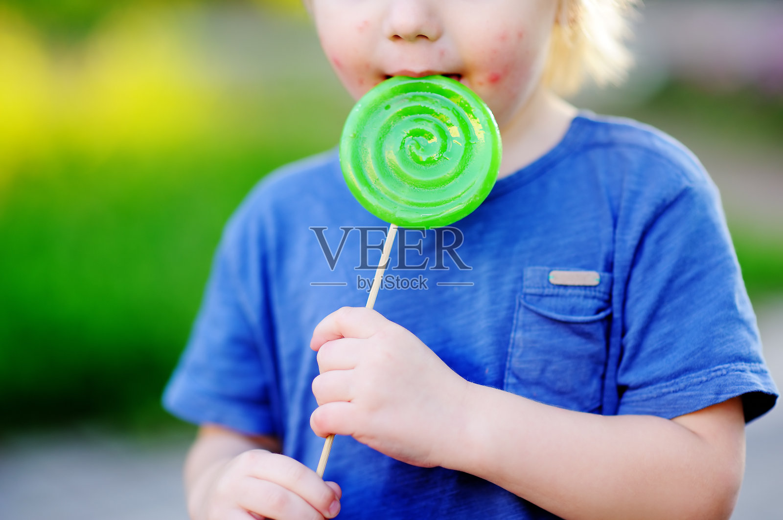 有过敏反应的孩子吃了大的绿色棒棒糖照片摄影图片