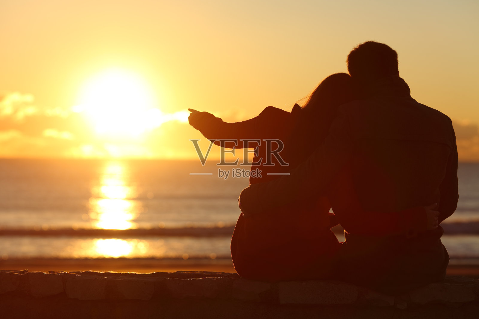 一对夫妇在冬天的海滩上欣赏日落照片摄影图片