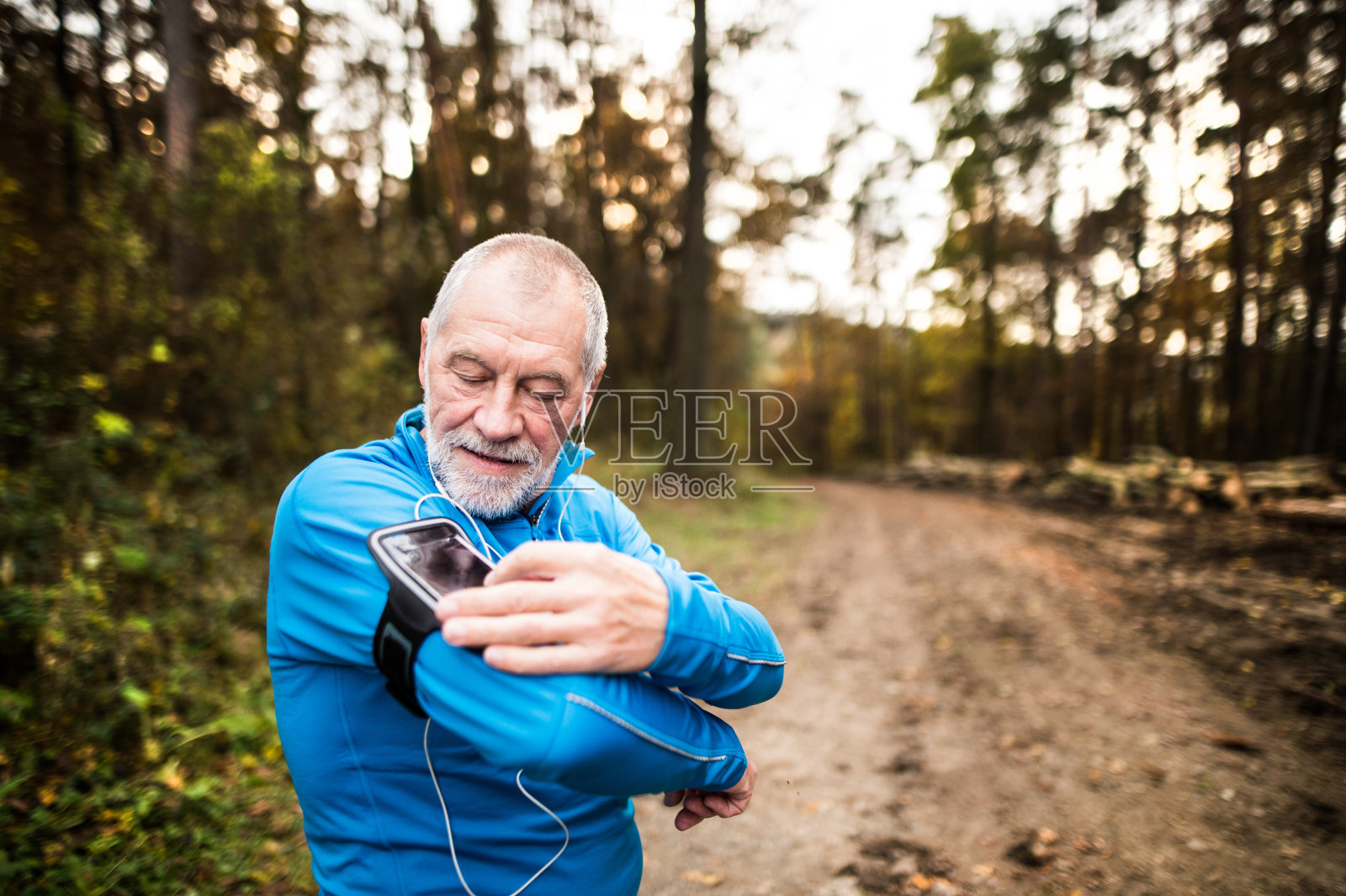 高级跑步者在自然与智能手机和耳机。照片摄影图片