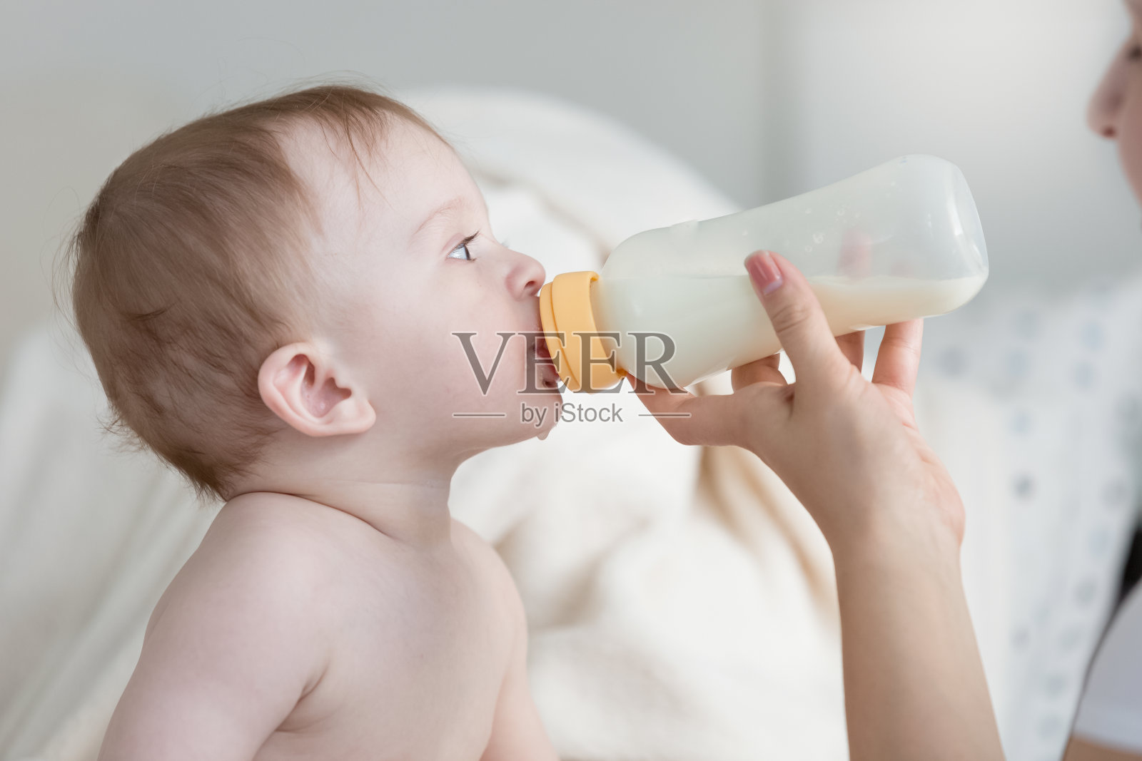 小男孩坐在床上，喝着奶瓶里的牛奶照片摄影图片