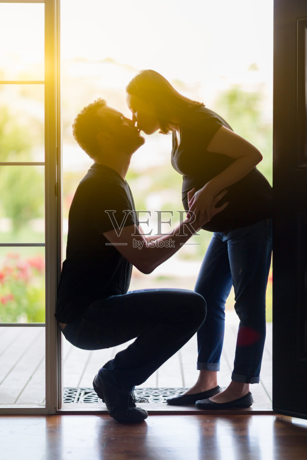混血怀孕夫妇在门口亲吻剪影。照片摄影图片