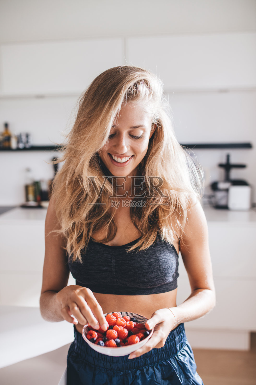 快乐的年轻女性在厨房吃浆果照片摄影图片