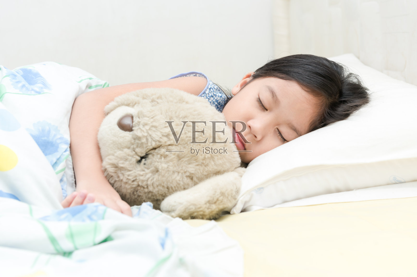 可爱的亚洲女孩睡觉和拥抱泰迪熊在床上。照片摄影图片