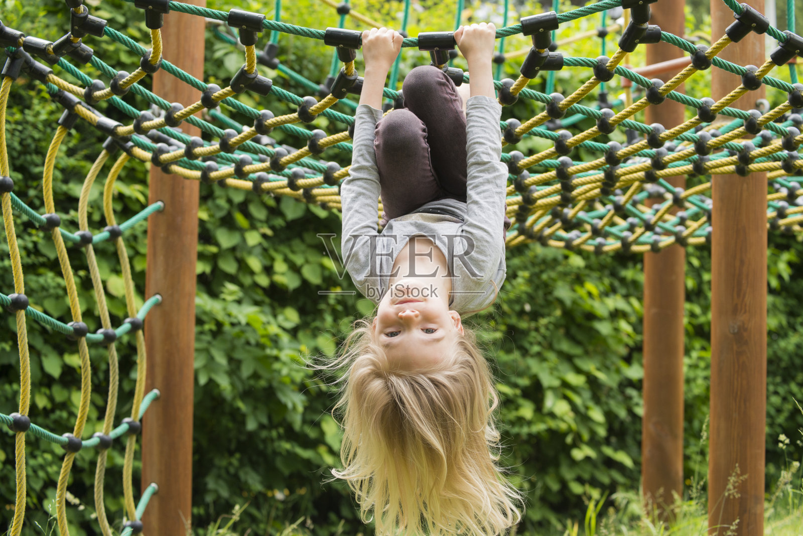 金发碧眼的小女孩在攀爬一根倒挂的绳子——夏天的游乐场照片摄影图片