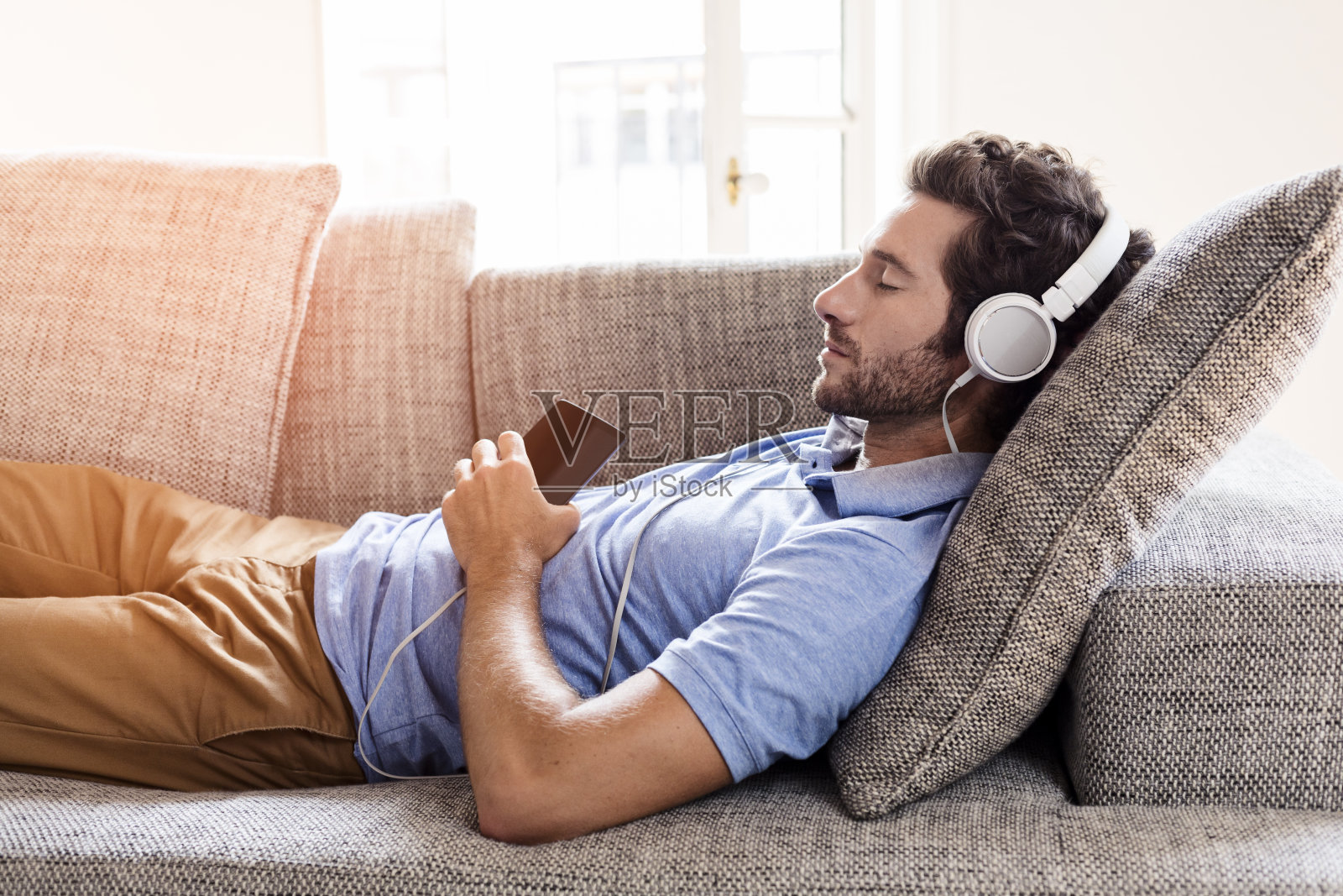 一个男人在沙发上用智能手机听音乐照片摄影图片