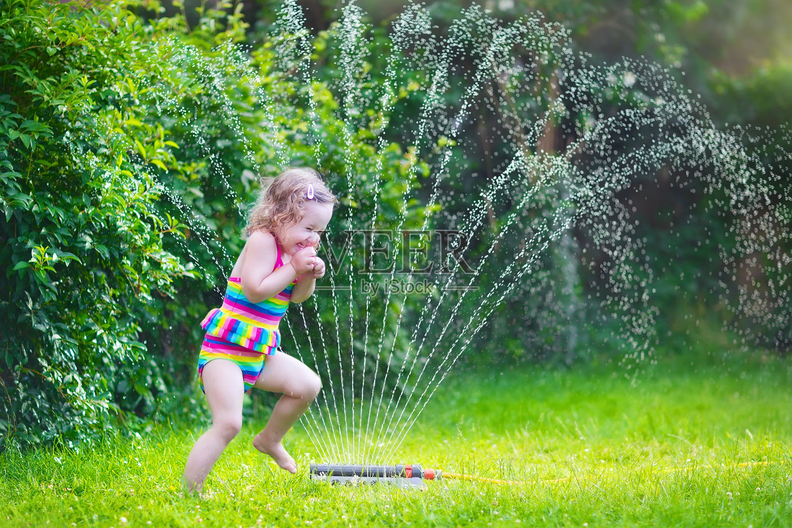 美丽的女孩玩花园洒水器照片摄影图片