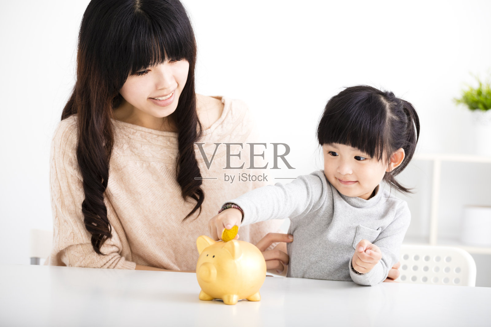 快乐的妈妈和女儿把硬币投进小猪储蓄罐照片摄影图片