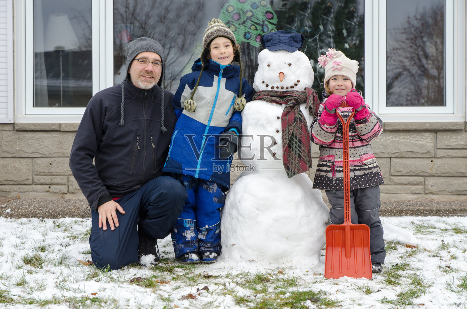 两个孩子和父亲在他们的第一个雪人旁边摆姿势照片摄影图片