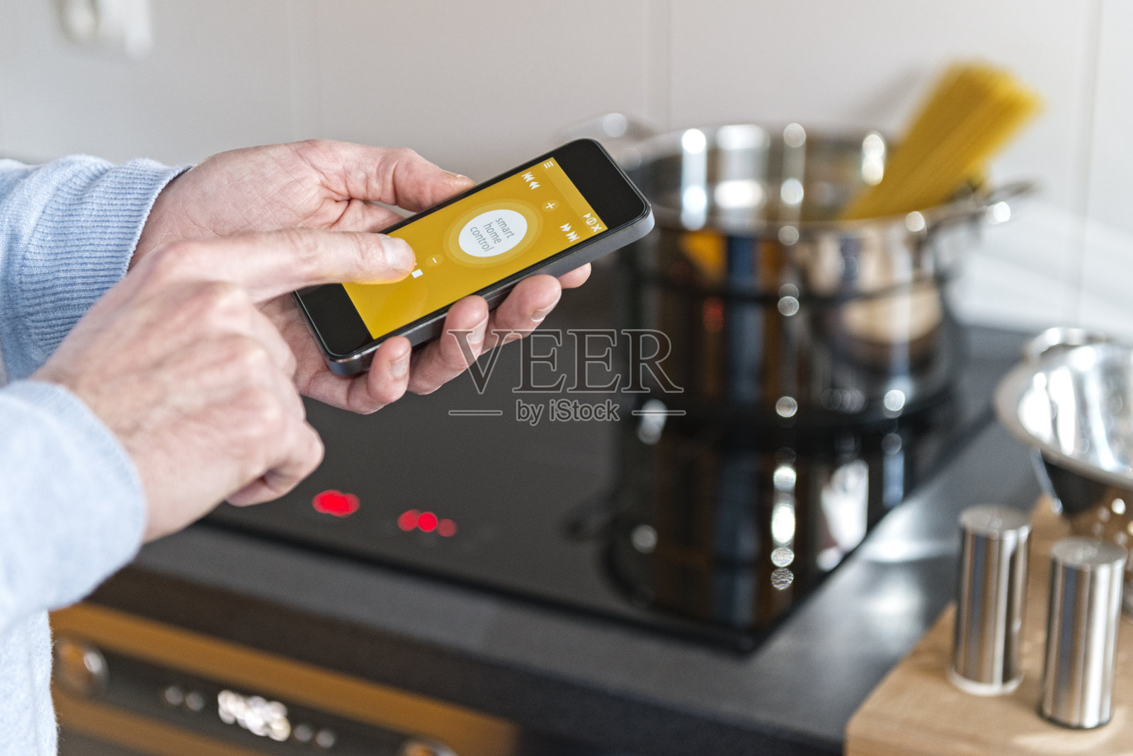男人手持手机智能控制家用炊具、厨房照片摄影图片