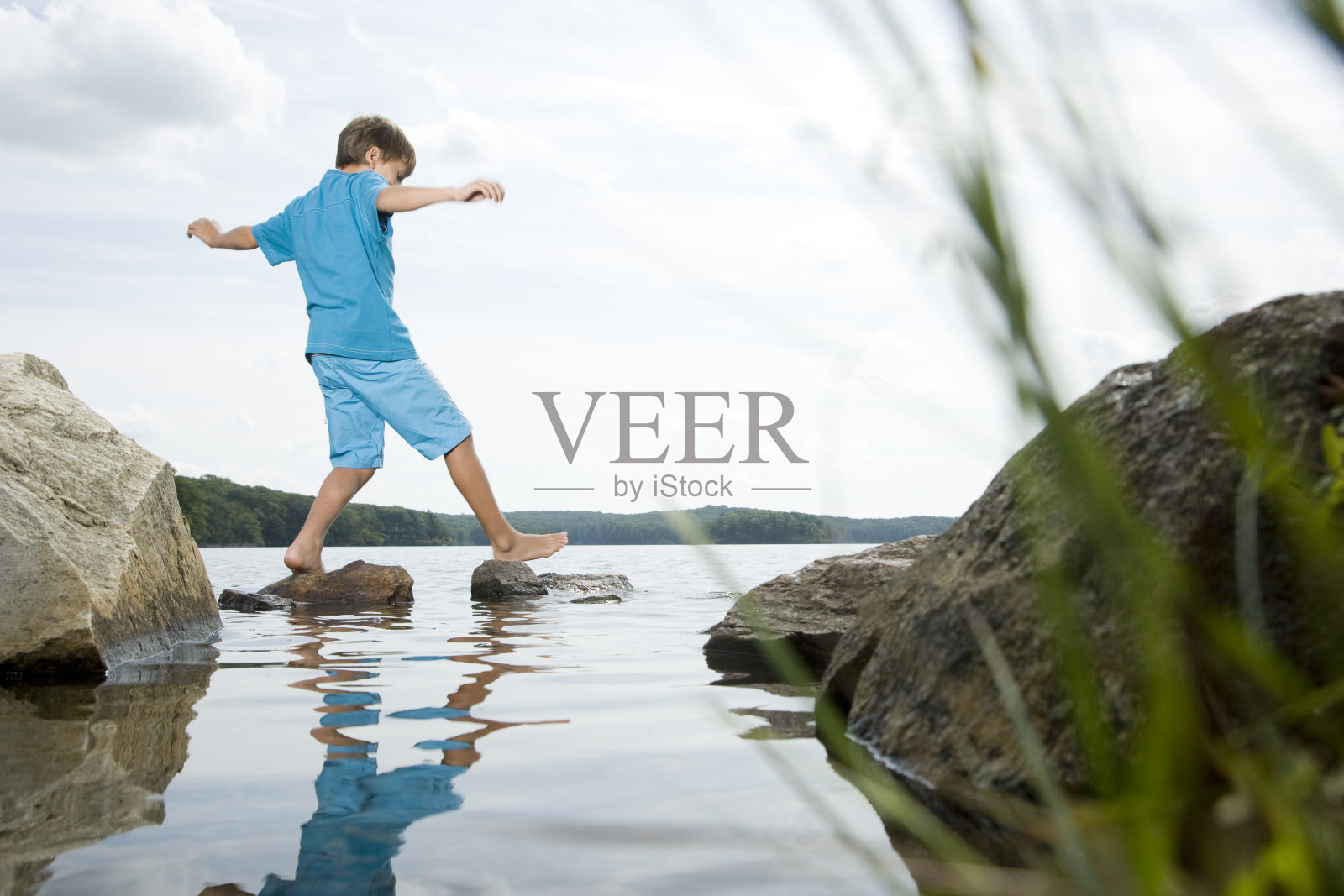 男孩光着脚走在湖里的石头上照片摄影图片