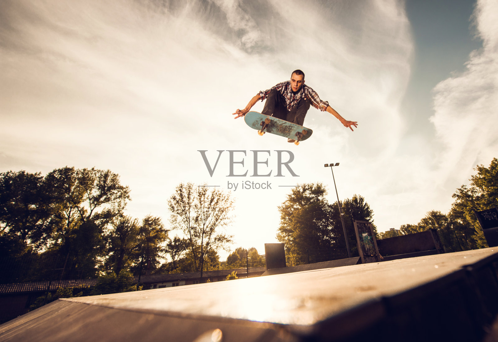 一个年轻人在日落时玩滑板的低角度视图。照片摄影图片