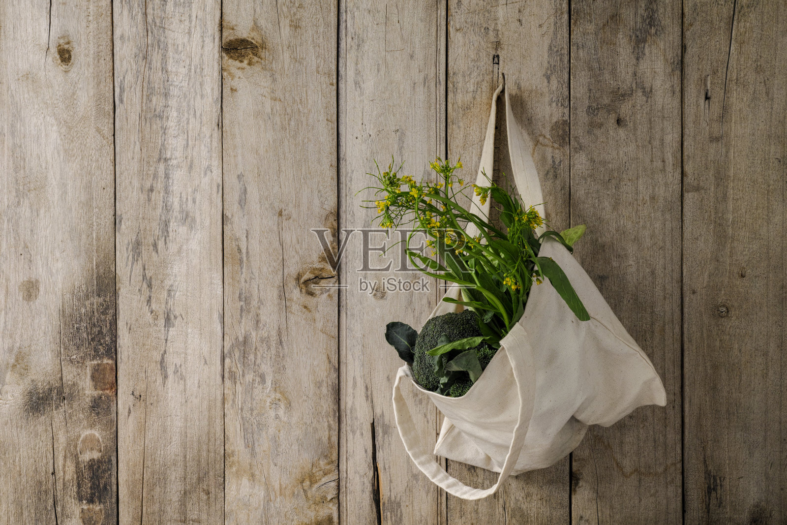 绿叶蔬菜装在一个天然棉花可重复使用的袋子里，挂在一个旧的风化的木板墙上。照片摄影图片