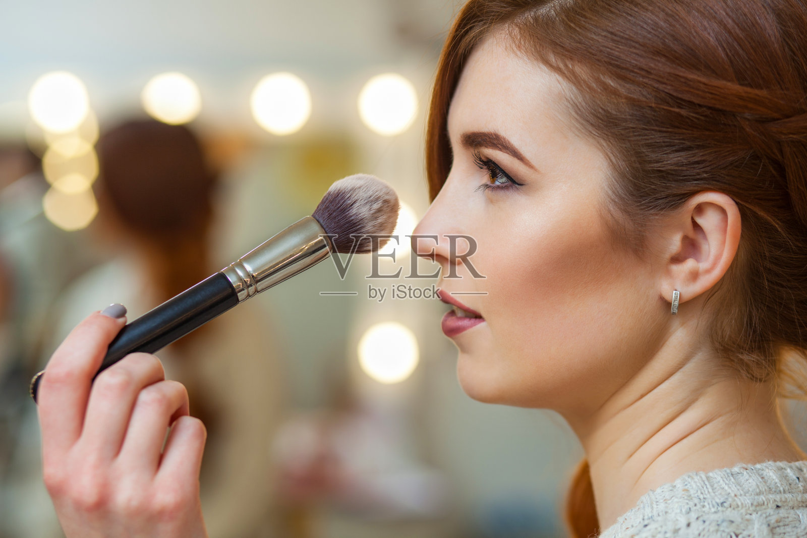 化妆师在一个漂亮的红发女孩脸上搽粉照片摄影图片