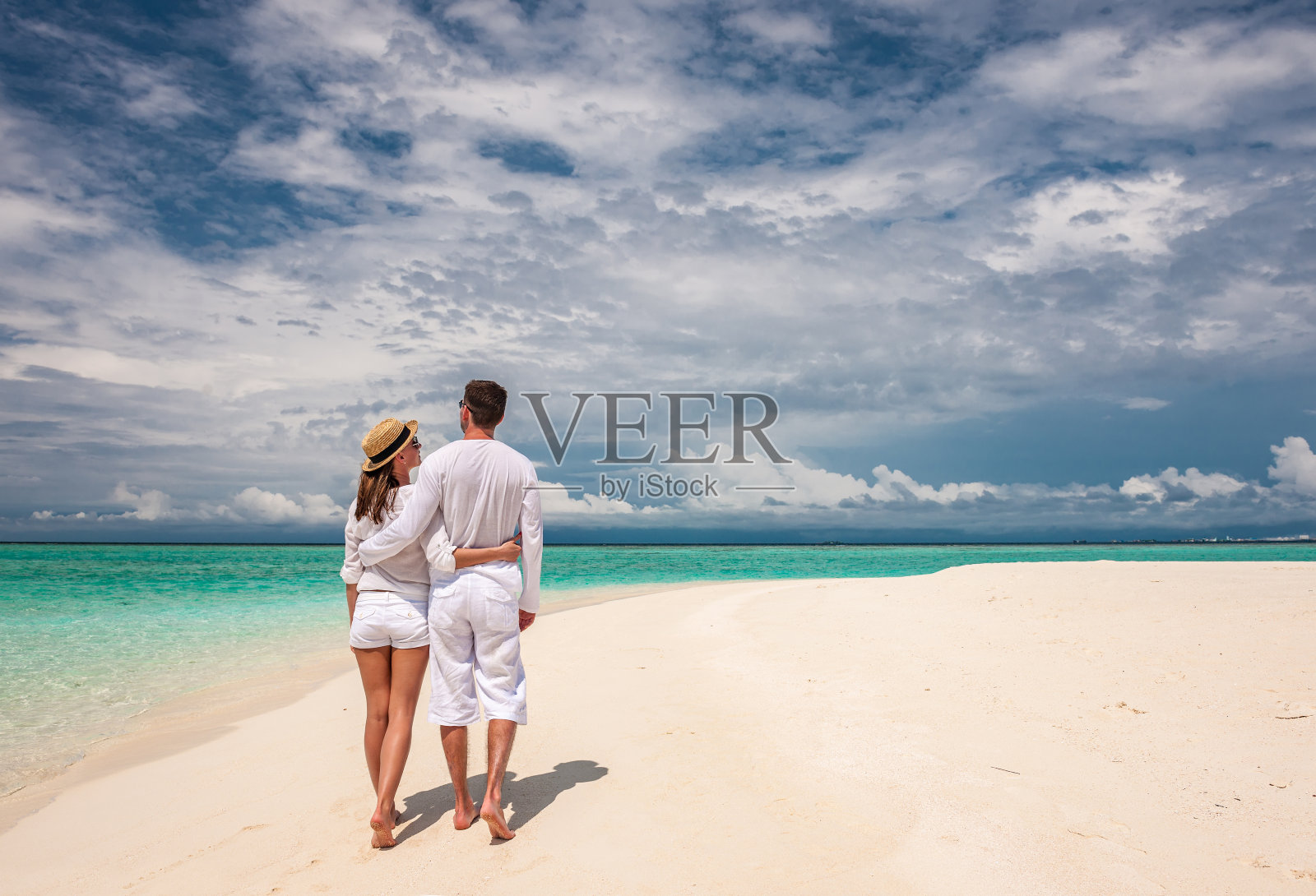一对穿着白色衣服的夫妇在马尔代夫的海滩上散步照片摄影图片