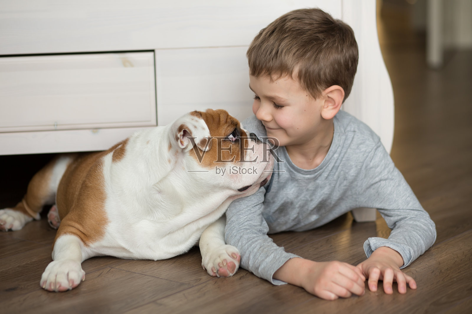 可爱的小男孩和英国斗牛犬的小狗在地毯上玩耍照片摄影图片