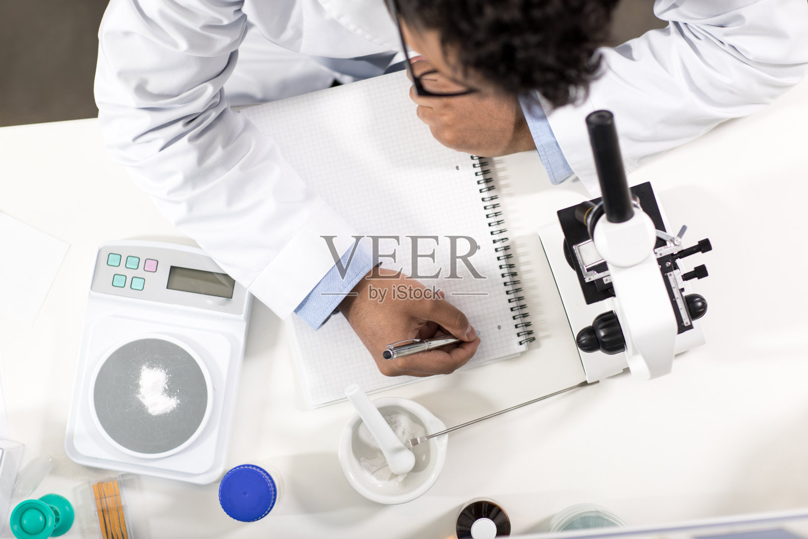 年轻科学家在实验室用显微镜工作和做笔记的俯视图照片摄影图片