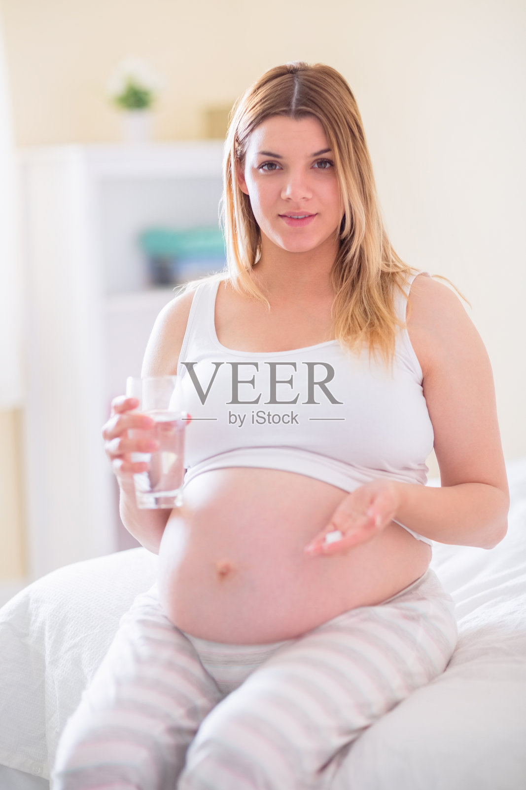 孕妇坐在床上，拿着一杯水照片摄影图片