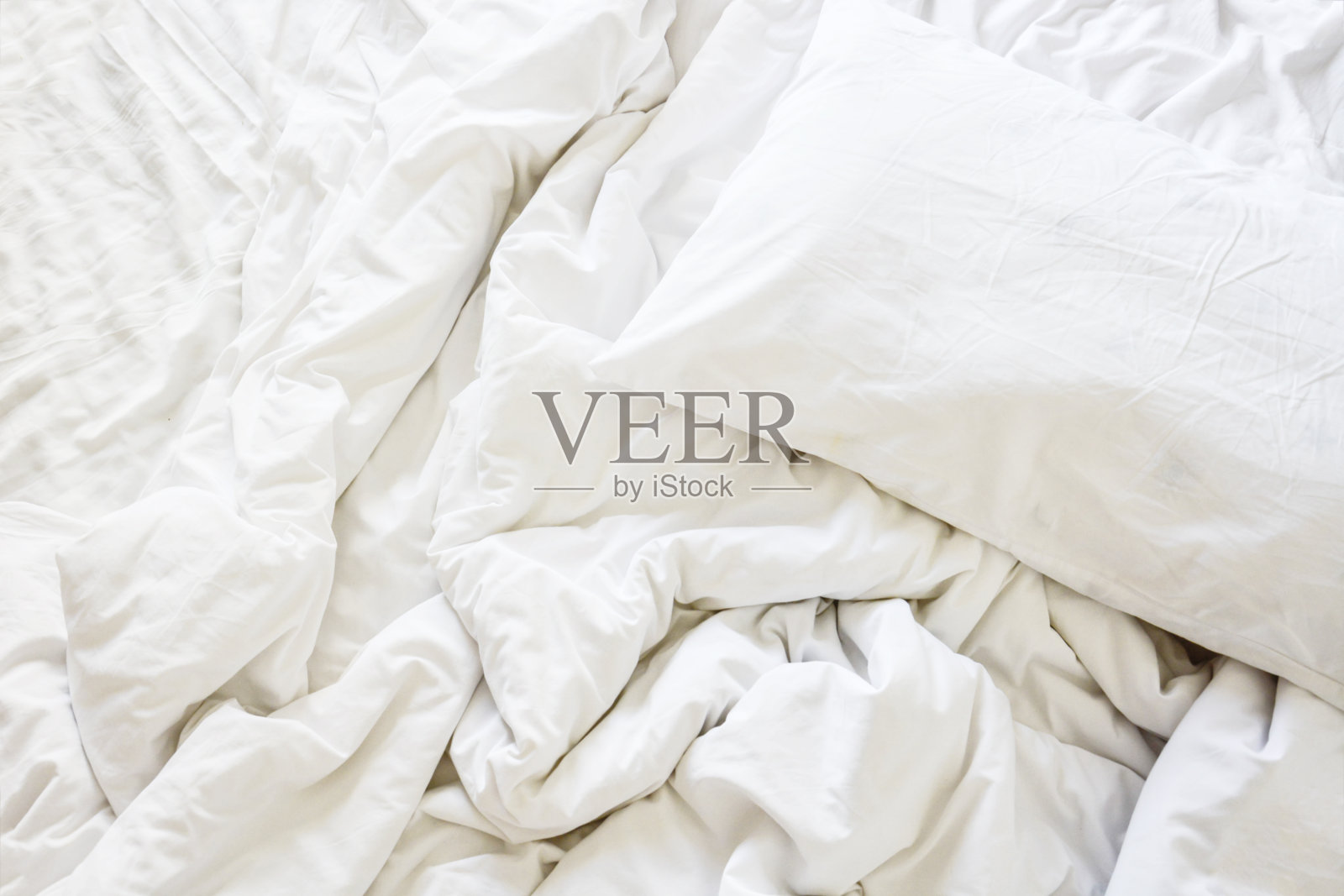 在床上放着白色的枕头和皱褶凌乱的毯子，早上醒来后躺在卧室里，睡了一个漫长的夜晚。照片摄影图片
