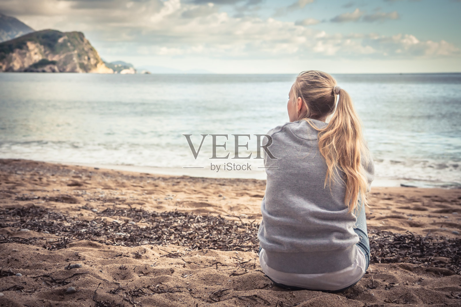 一个忧郁孤独的年轻女子坐在海滩上，抱着膝盖，满怀希望地望着远方照片摄影图片