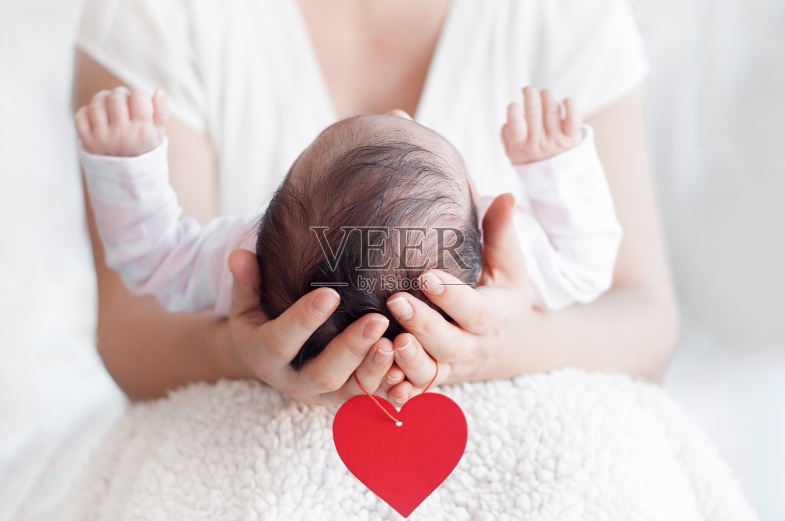 母亲双手抱着新生婴儿的头。幸福的家庭的概念。母爱和父母之爱。红心挂在胳膊上。照片摄影图片