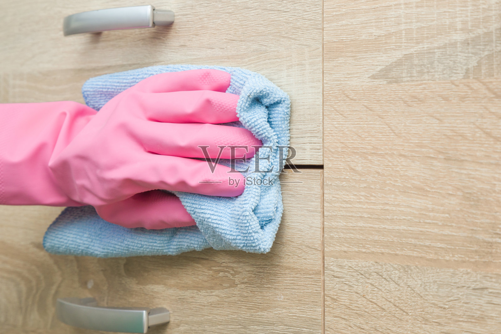 手拿粉红色橡胶防护手套，用抹布擦拭房间里的碗柜。早春大扫除或定期大扫除。女保洁员打扫房子。照片摄影图片
