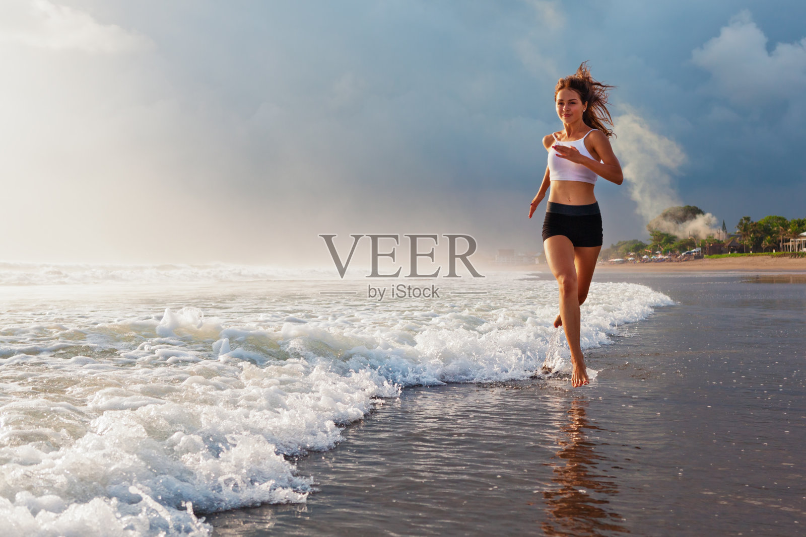 活跃的运动女人沿着日落的海洋海滩跑步。运动背景。照片摄影图片