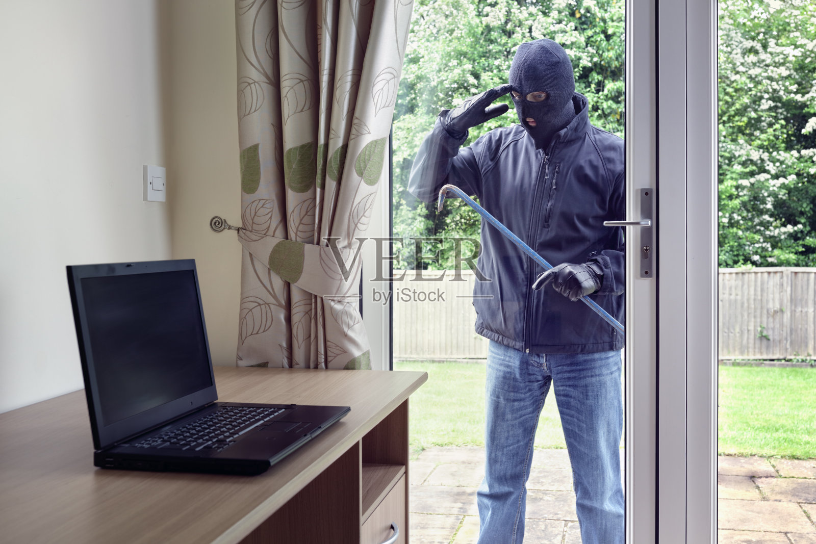 小偷从露台的门窗口望向一台笔记本电脑去偷照片摄影图片