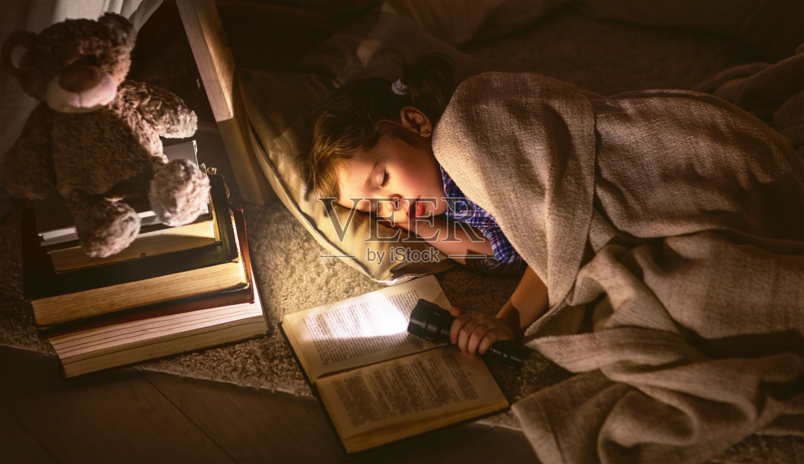 小女孩睡在帐篷里，带着书和手电筒照片摄影图片