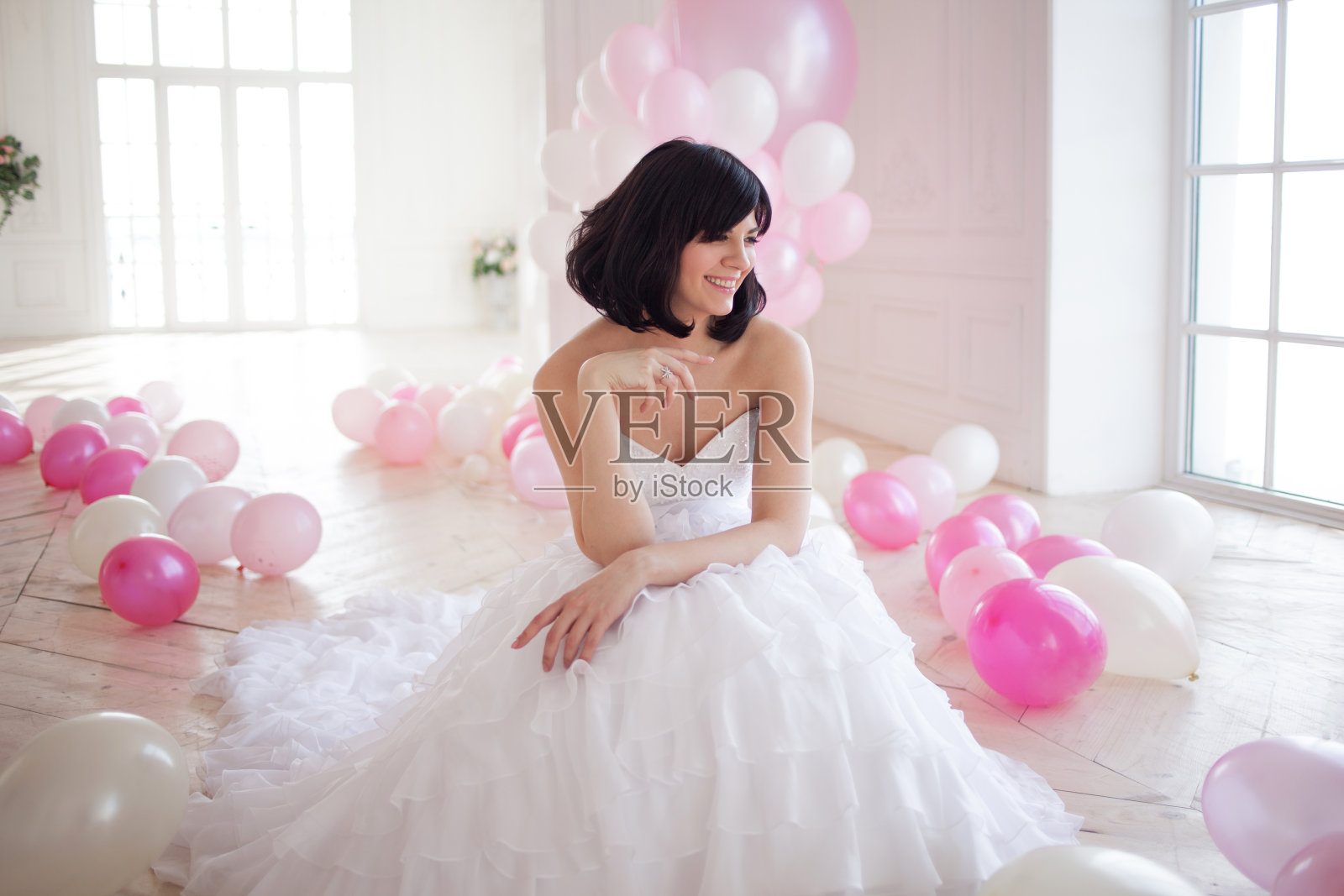 穿着婚纱的年轻女子在奢华的室内装饰着一堆粉色和白色的气球。照片摄影图片