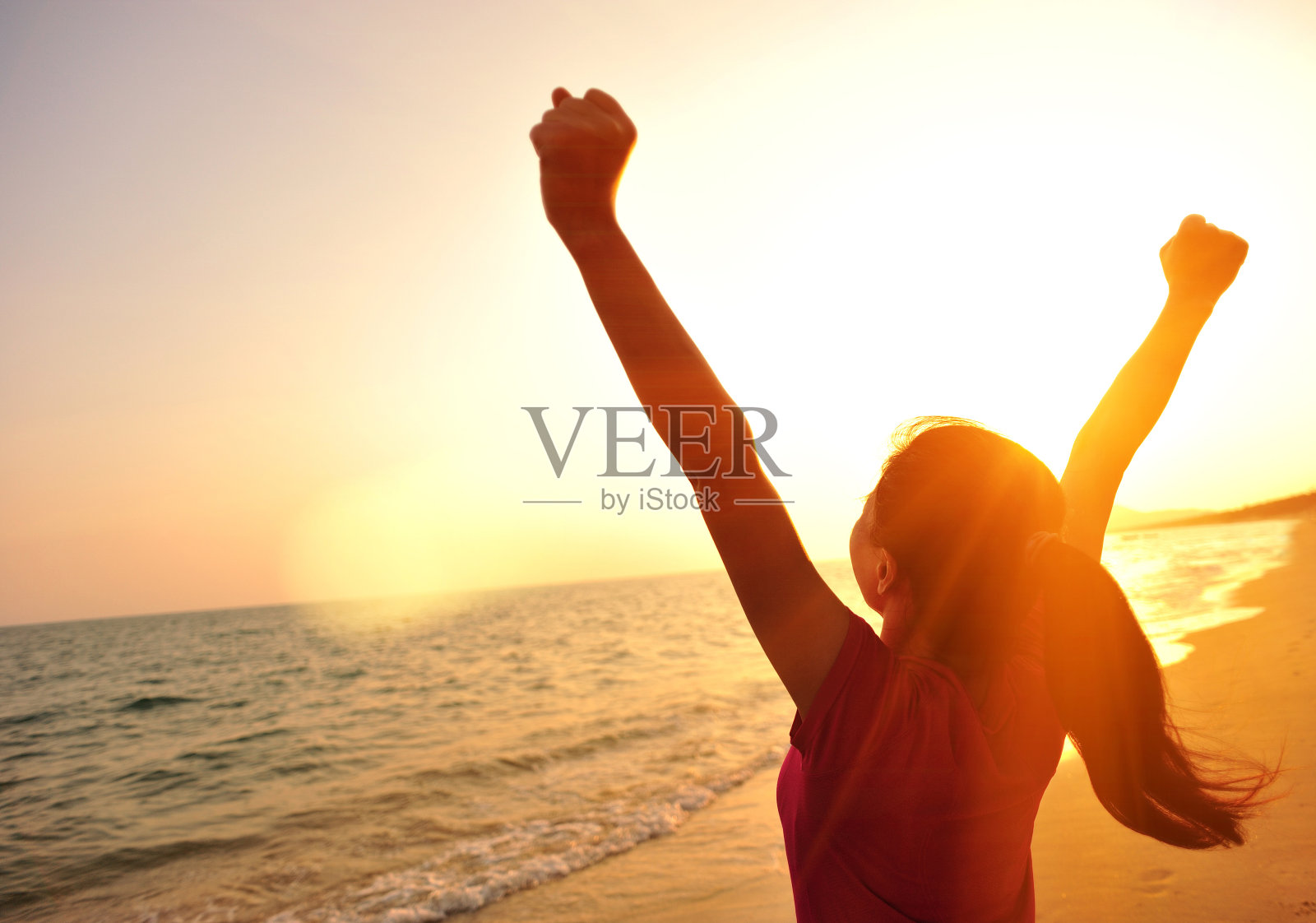 欢呼的女人在海边向夕阳张开双臂照片摄影图片