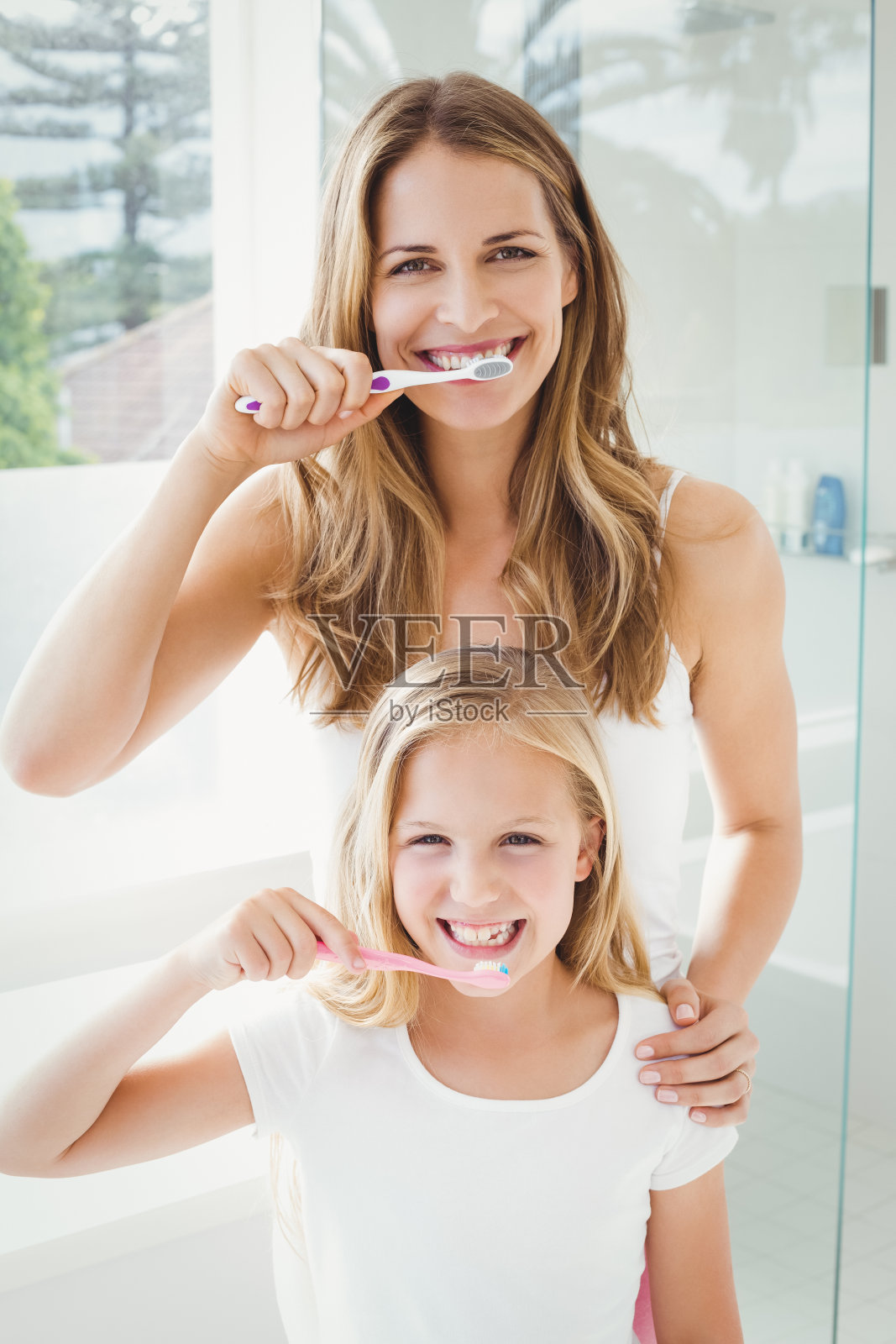 微笑的母亲和女儿刷牙的肖像照片摄影图片