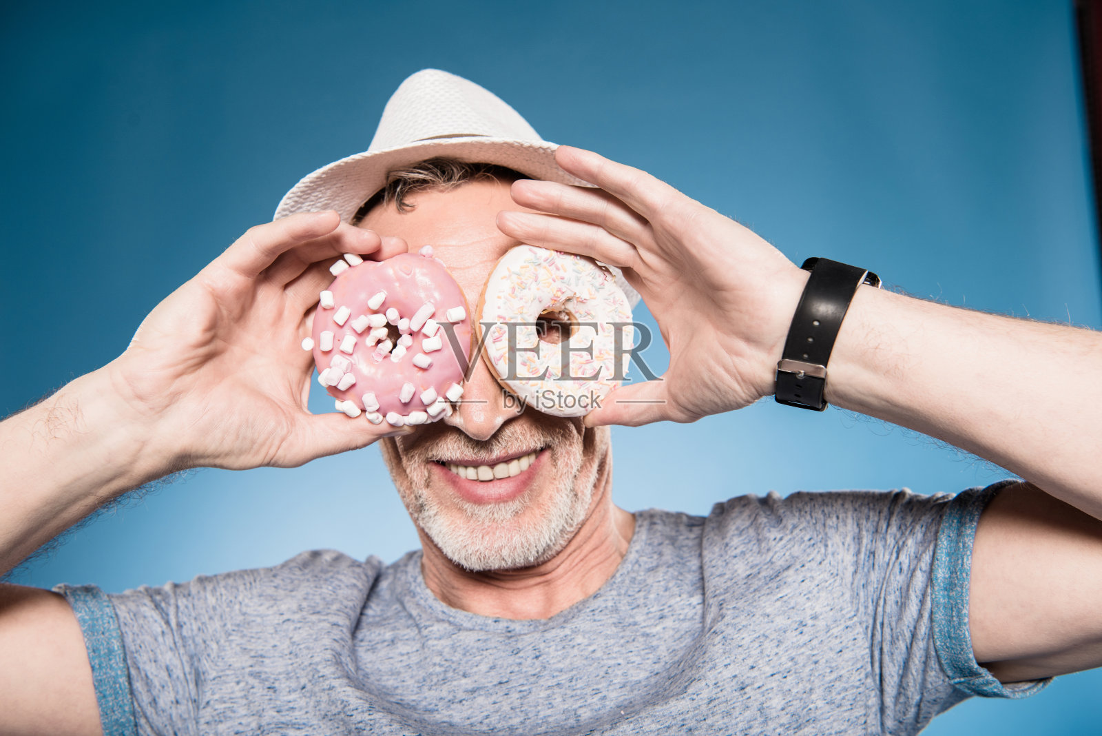 一个随意的老人在眼前拿着甜甜圈的肖像照片摄影图片