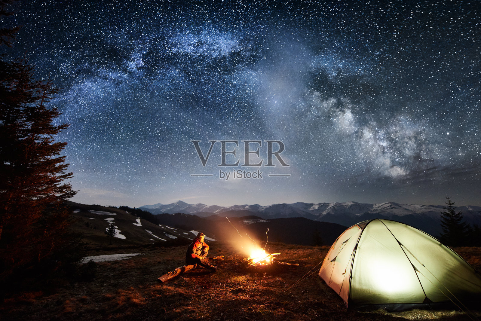 男游客在森林附近的营地里享受夜晚。在满是星星和银河的美丽夜空下，一个人坐在篝火和帐篷旁。天体摄影术照片摄影图片