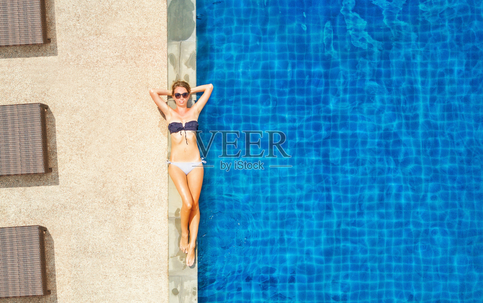 年轻女孩在比基尼和太阳眼镜晒太阳接近游泳池，俯视图照片摄影图片