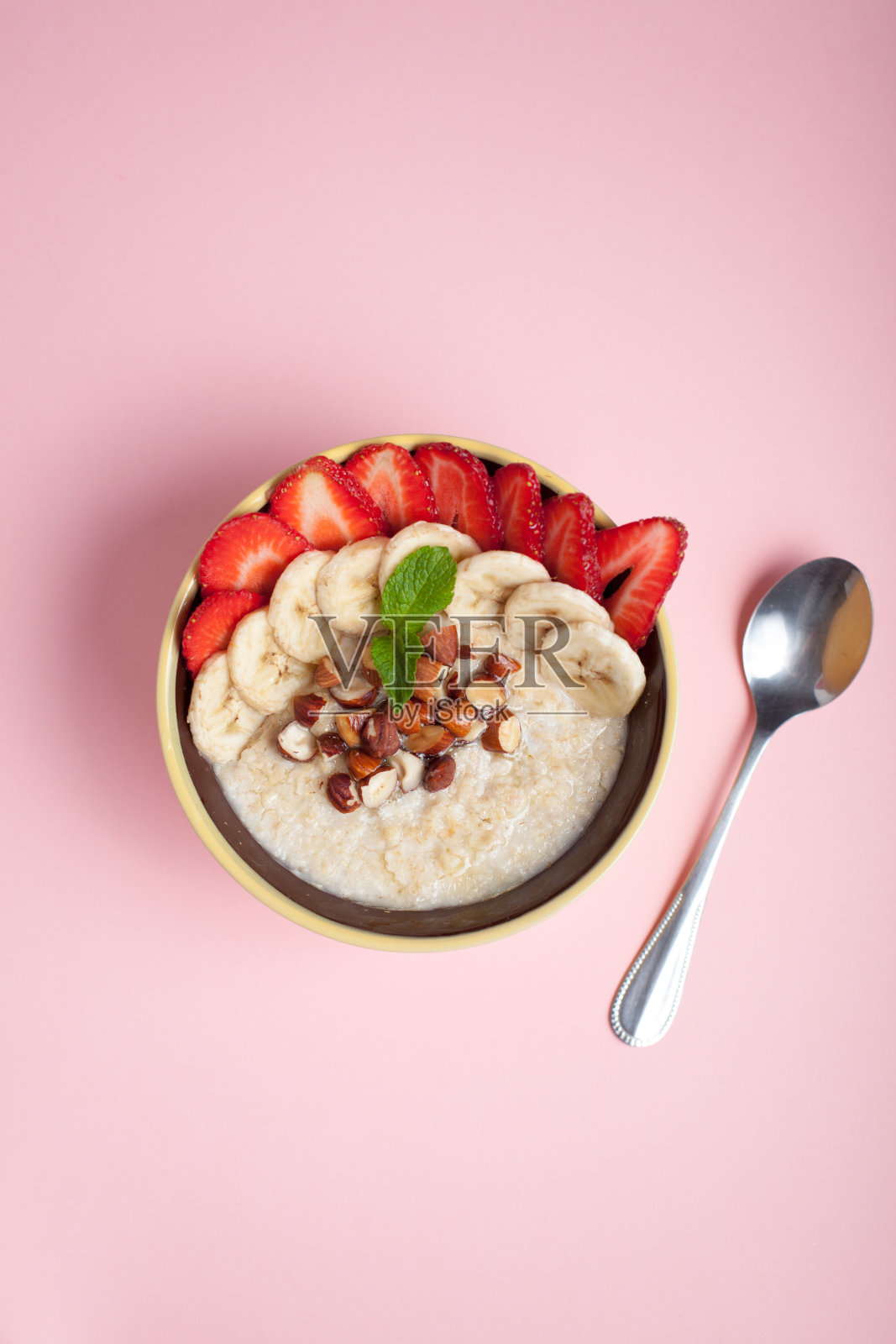 一碗有香蕉、草莓、杏仁、榛子和奶油的粉色燕麦粥。热腾腾的健康早餐，俯视图照片摄影图片
